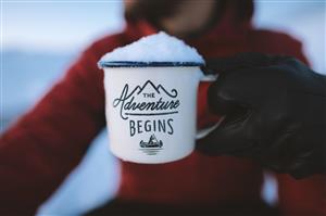 Snowfilled coffee cup that says Adventure Begins